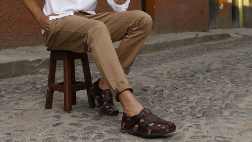 Hombre elegante con sandalias de lujo para hombre en un entorno veraniego mediterráneo, junto a una piscina o paisaje costero